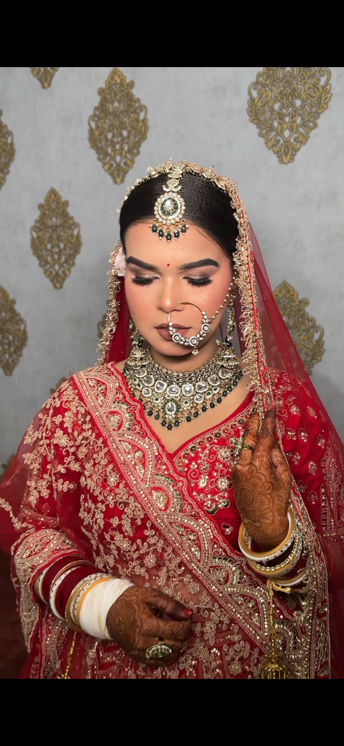 Traditional bride with ornate gold nath and emerald choker in deep red lehenga