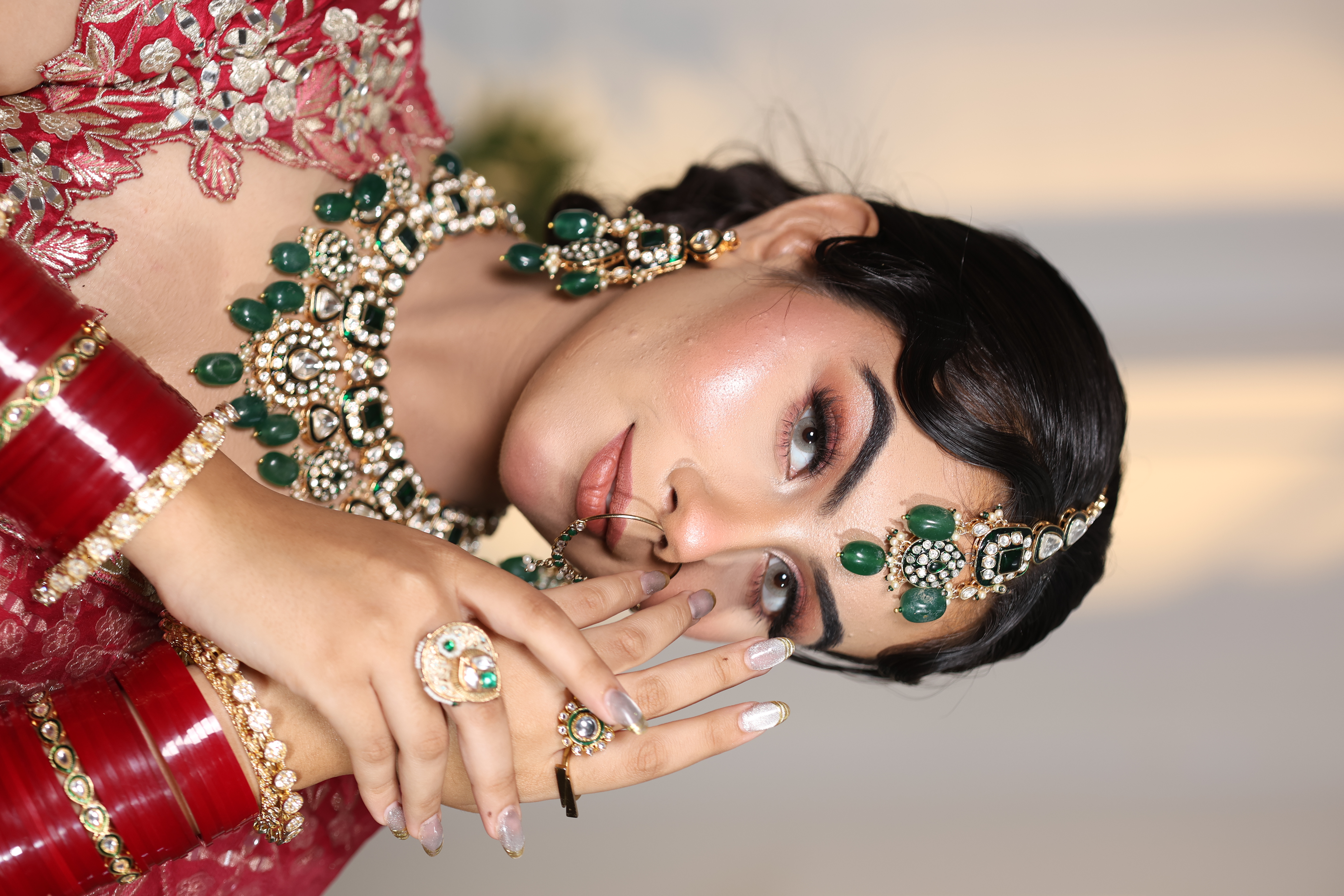 Editorial bride in heavy red zardozi lehenga wearing emerald jewellery and gold nath