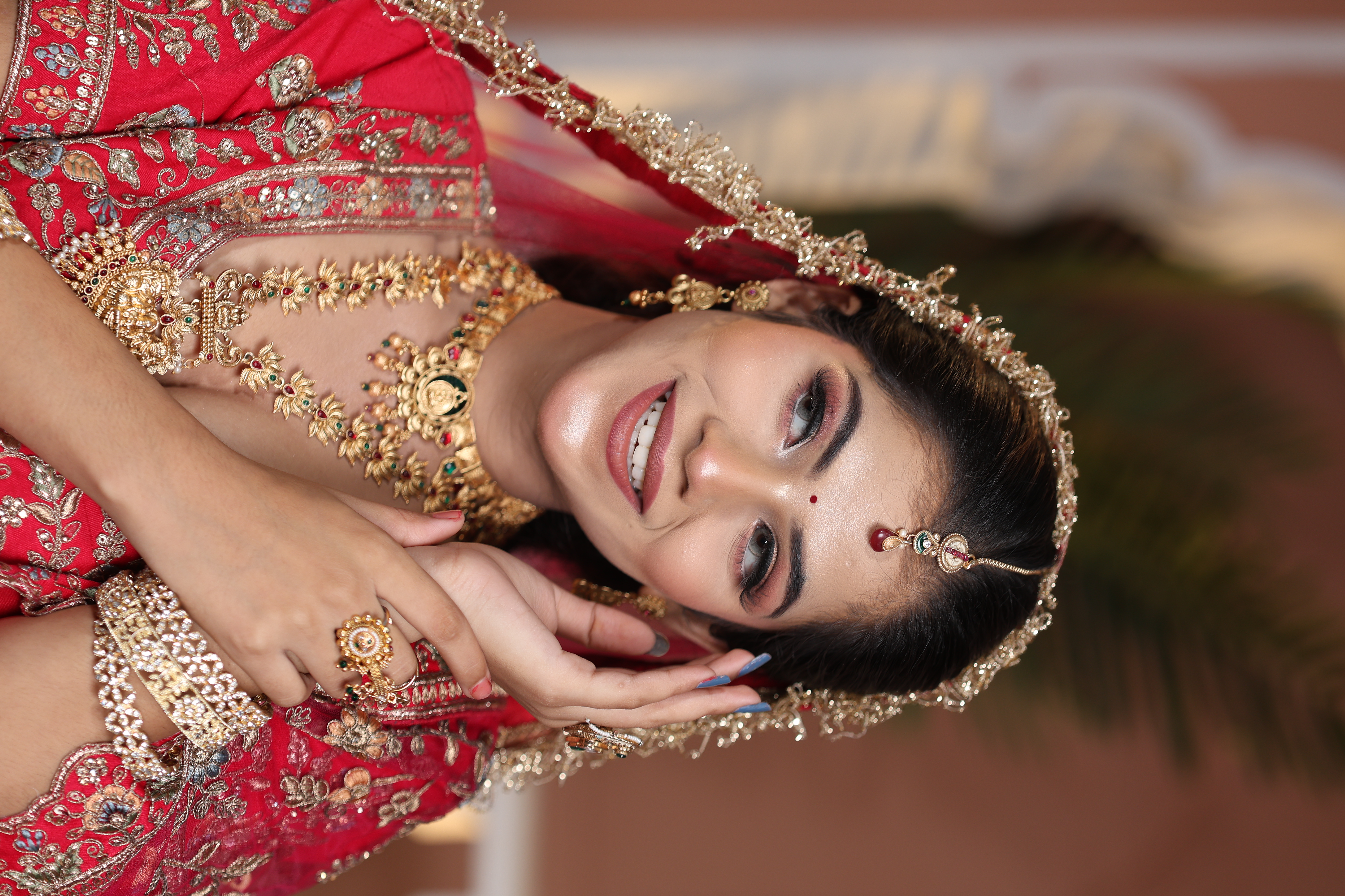 Radiant smiling bride in red and gold embroidered lehenga with delicate temple jewellery